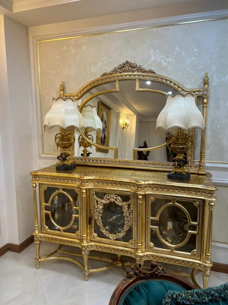 آینه کنسول نگینی از برند صنایع چوب رادین ساخته شده از چوب راش طبیعی با طراحی کلاسیک و نگین‌کاری زیبا، مناسب دکوراسیون لوکس منزل و سالن پذیرایی، دارای آینه کریستال شفاف و روکش براق در رنگ‌های طلایی و سفید صدفی.